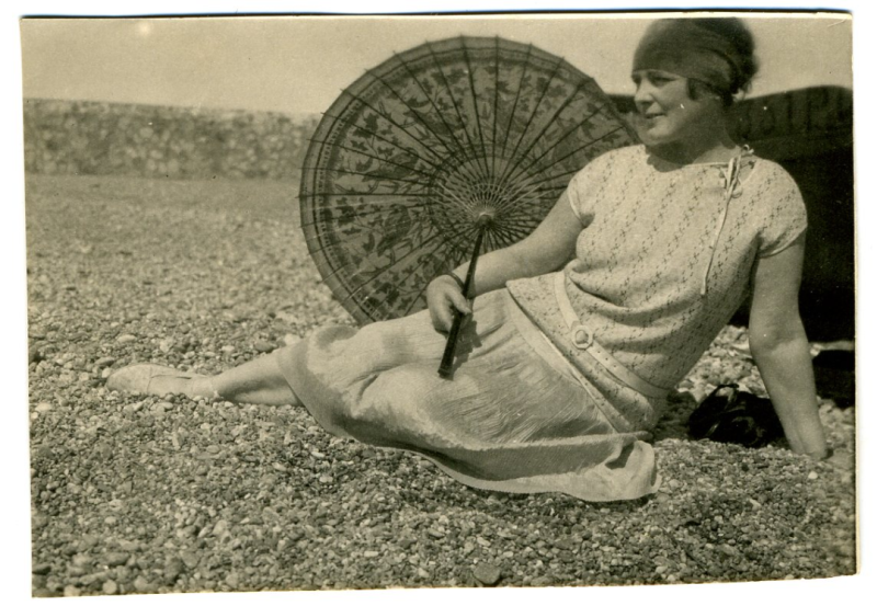 Czarno-białe zdjęcie siedzącej kobiety z parasolem na kamienistej plaży 
